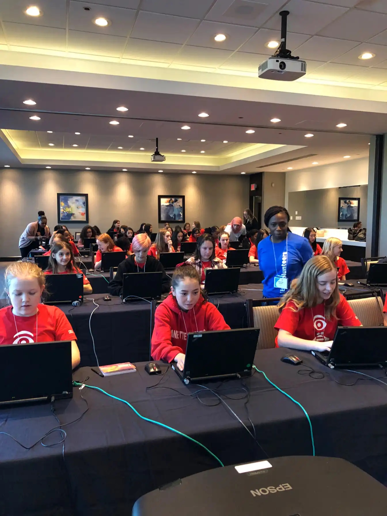 Salle de classe avec des participantes au CyberDay4Girls travaillant sur des ordinateurs portables et des mentors aidant les élèves.