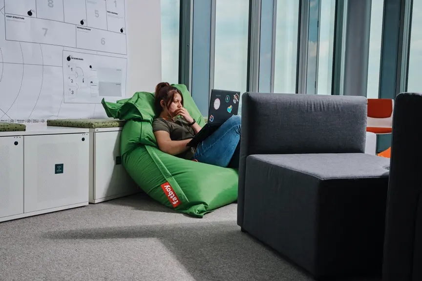 Femme travaillant sur un ordinateur portable, assise dans un fauteuil en forme de sac à haricots au bureau.