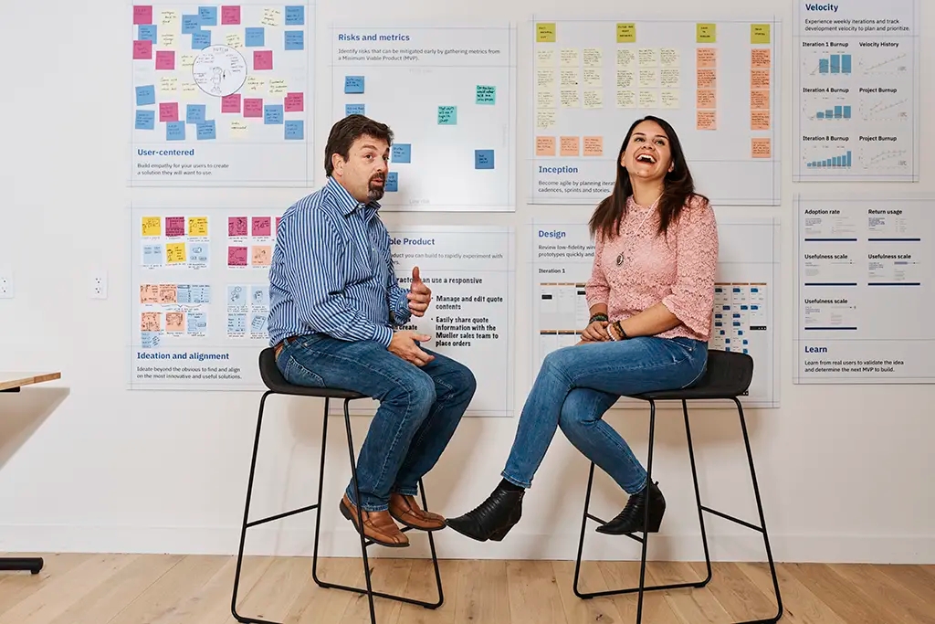 Two people sitting in front of sticky note boards presenting at a design thinking workshop
