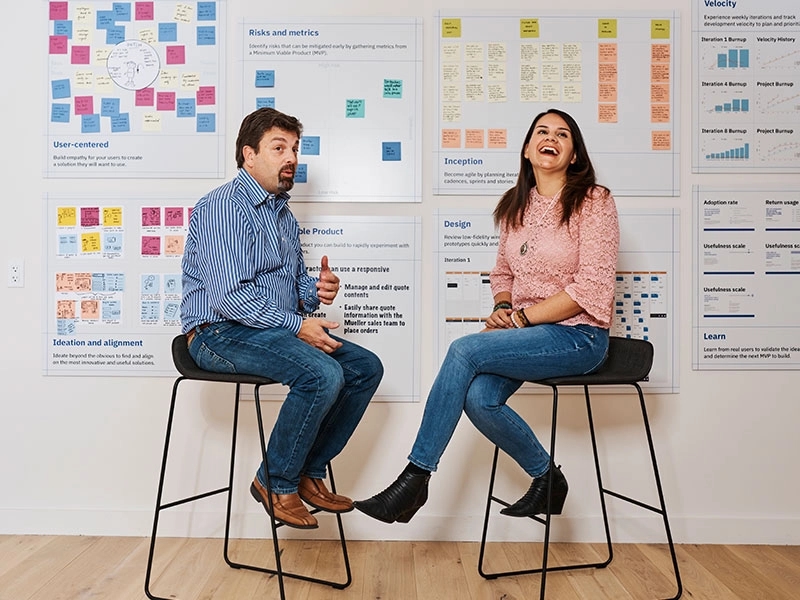 Dos personas sentadas frente a tableros de notas adhesivas durante una presentación en un taller de pensamiento de diseño
